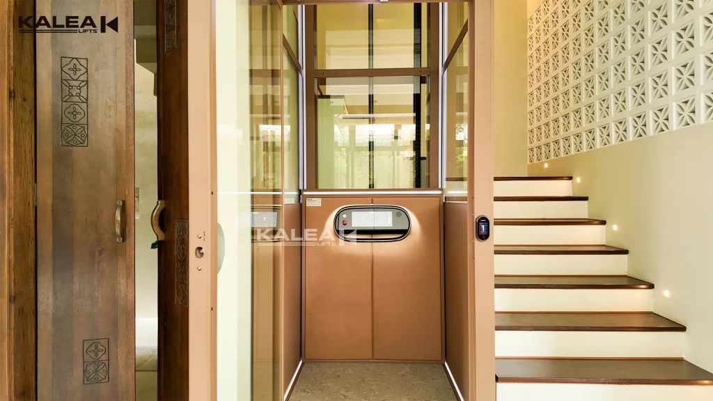 Tampilan depan lift rumah Kalea dengan pintu kaca di samping tangga
