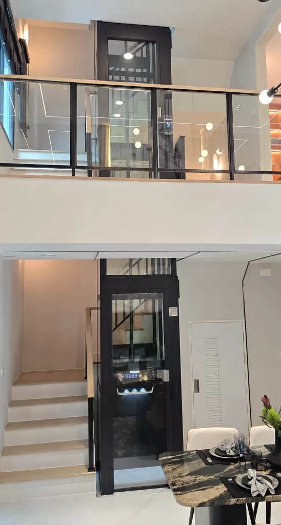Lift rumah platform Kalea KOSMOS dengan rangka hitam dan panel kaca terpasang di rumah dua lantai modern, tampak dari lantai atas dan lantai dasar 